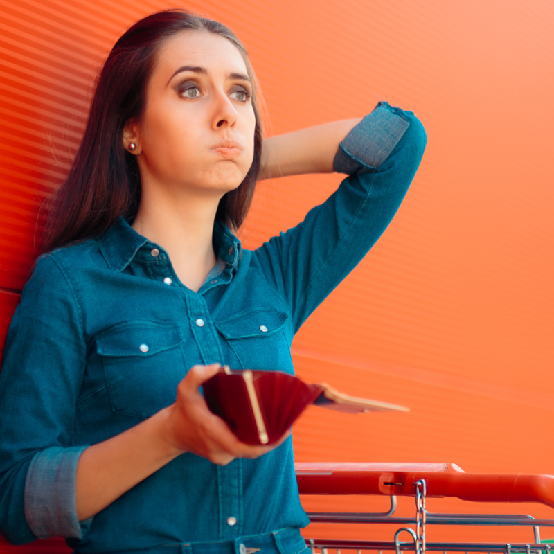 women leaning against an orange wall with a supermarket trolley and a purse in her hand